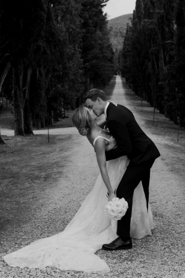 Photo of the newlyweds kissing with dip along the cypresses lined road to Borgo Stomennano