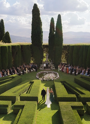 Bride walks down the aisle with her parents in an iconic garden wedding ceremony at La Foce