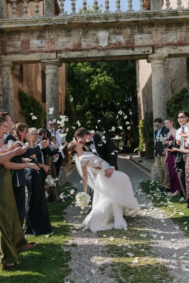 Wedding ceremony recessional: bride and groom kiss while guests toss petals on them.