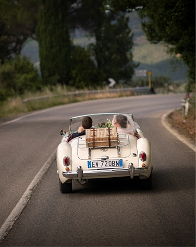 Elopement in Tuscany: bride and groom driving a convertible car through the rolling hills.