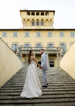 Bride and groom look back on stairs in front of Villa di Maiano facade