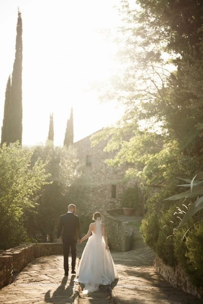 Bride and groom walk around the wedding venue holding hands with the sun shining through