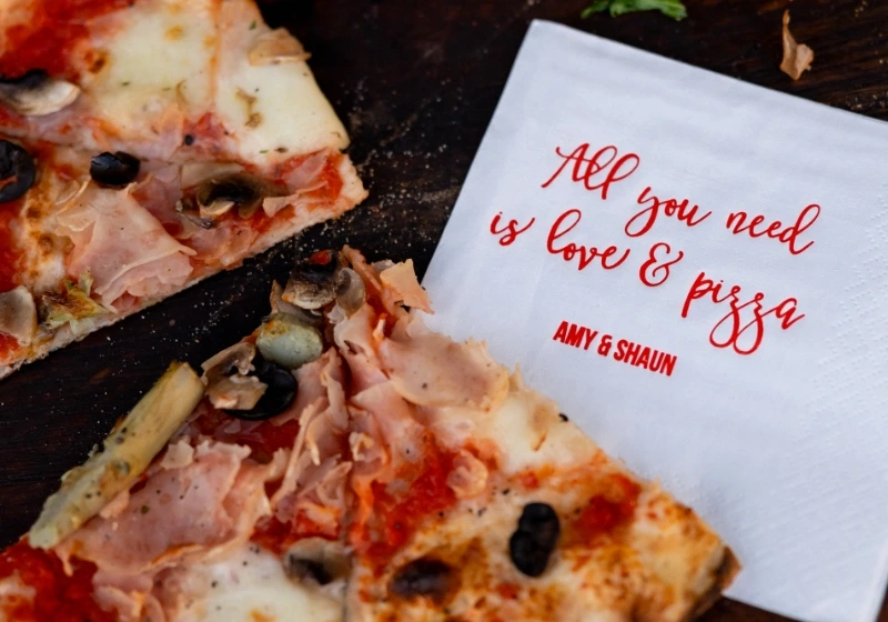 Wedding welcome party in Tuscany: pizza close-up with message 'all you need is love and pizza' on napkin