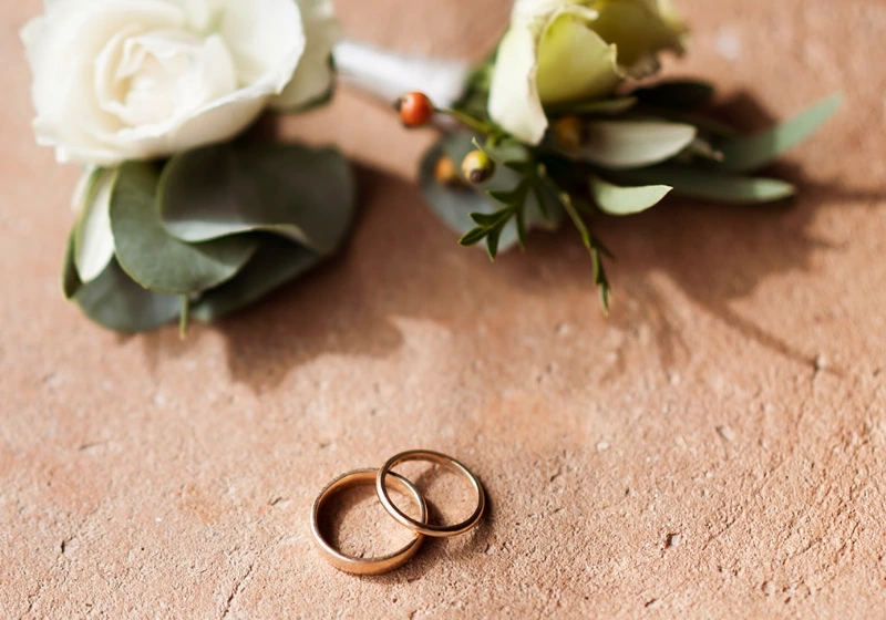 Detail shot of wedding bands with buttonholes made of white flowers and greenery