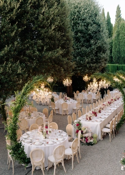 Overview of outdoor wedding dinner recpetion with round tables and crystal chandeliers hanging from arches 