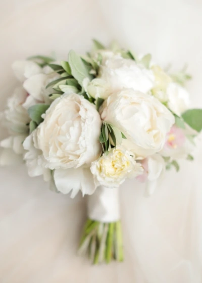 Close up of white bridal bouquet made of white peonies and greenery 