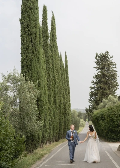 Bride and groom walking hand in hand along the tree-lined avenue of Villa Medicea dililliano